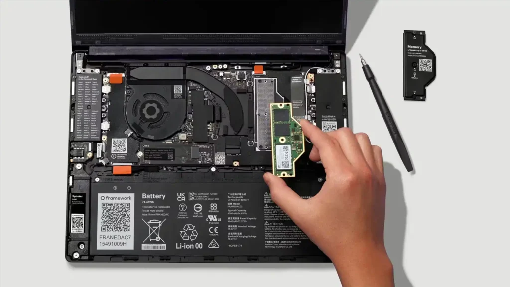 Framework Laptop 13 Pro open chassis with user installing memory module into slot using hand and screwdriver nearby, showcasing upgradeable and modular design