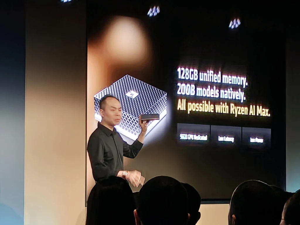 Presenter holding AMD Ryzen AI Halo Box during AI event presentation showing 128GB unified memory and AI capabilities