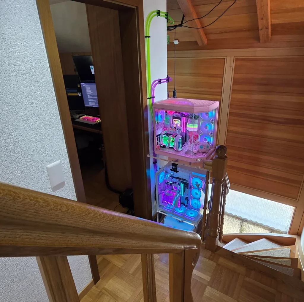 Two stacked gaming PCs connected to a shared external liquid-cooling system beside a staircase