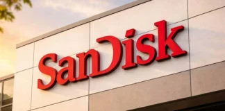 16-Year-Old SanDisk 64GB SSD Passes 1 Petabyte of Writes, Beating Warranty by 25x SanDisk sign photographed against a clear blue sky, partially obscured by green leaves in the foreground.