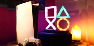 Sony CEO Hints at $1,000 Pricing for PlayStation 6 A gaming desk setup featuring a PlayStation 5 console, DualSense controller, and a glowing PlayStation symbols light.