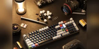 QwertyKeys QK100 Mk2 Mechanical Keyboard Launches at $219 Lifestyle desktop setup showing QK100 Mk2 mechanical keyboard with keycaps, switches, camera lenses, and a controller.