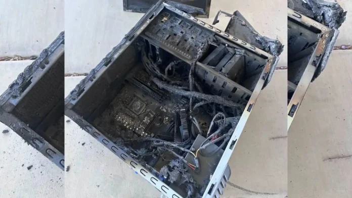 A 16:9 padded layout showing a completely burned out computer chassis with charred motherboards and melted power cables lying on a concrete floor.