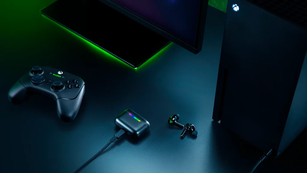 Lifestyle view showing the black Razer Hammerhead V3 X HyperSpeed for Xbox earbuds next to an Xbox controller and console.