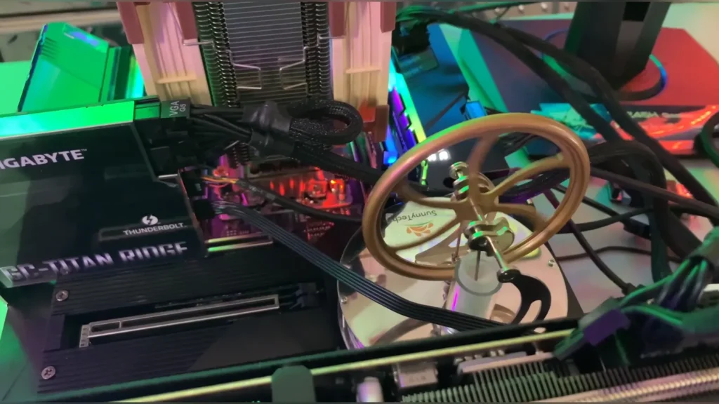 A miniature Stirling engine with a golden flywheel spinning inside a PC chassis next to a Gigabyte GC-Titan Ridge expansion card.