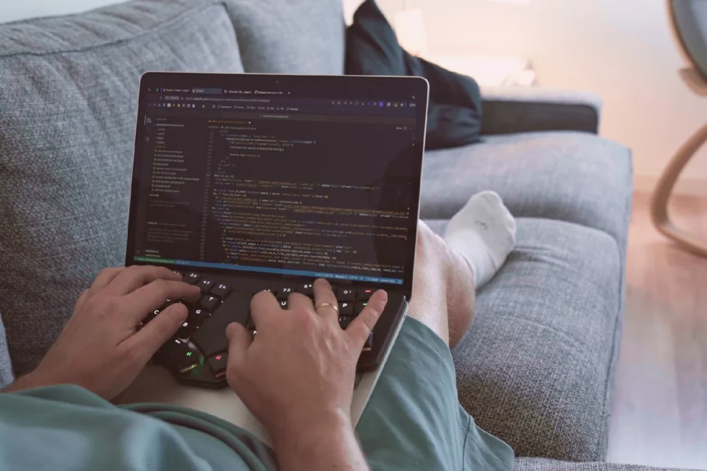 Dygma Releases Sonsei Travel-Friendly Ergonomic Mechanical Keyboard 5 User typing on the Dygma Sonsei ergonomic keyboard while working on a laptop from a sofa.